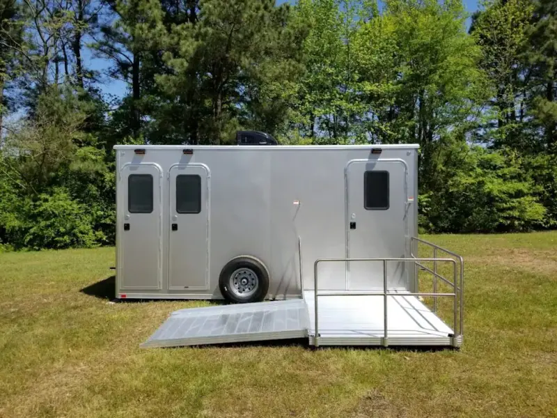 Silver ADA restroom trailer with two doors and a ramp on grass