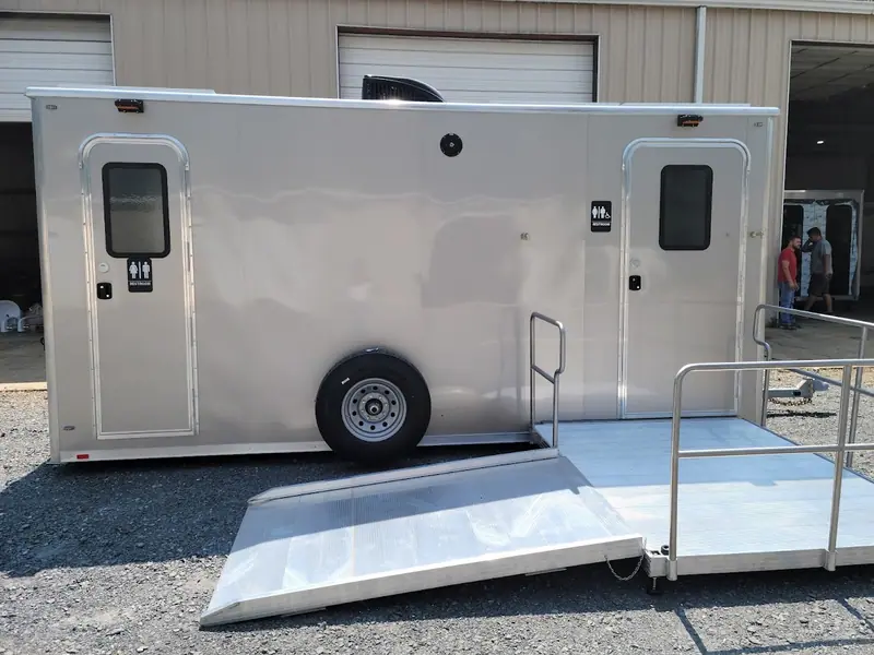 Silver ADA restroom trailer with a ramp outside a metal shop building