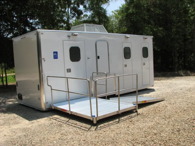 Large ADA restroom trailer with a wide ramp and railings on gravel