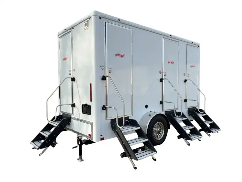 The 4 Person Station Restroom Trailer (16’ x 6’) features multiple entry doors, metal staircases, and a wheeled base with support stands—ideal for events requiring a portable restroom solution.